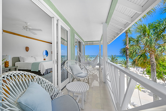 bedroom with white linens, light blue quilt draped at end of bed, and double doors leading to an outdoor terrace