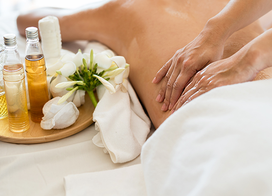 woman getting a back massage at the spa with a tray of spa treatments on the bed