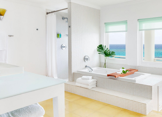 bathroom area with white tile tub and shower area, windows overlooking the ocean, and vanity area