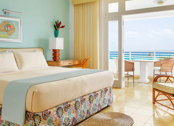 guest room with light yellow and light blue accent colors and a balcony area overlooking the ocean