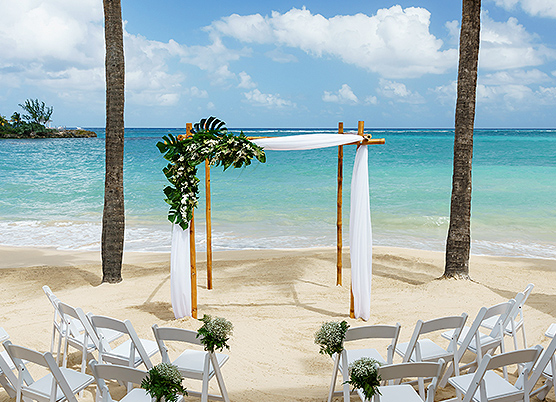 an ocean front beach wedding ceremony set with with a small gazebo draped with white tulle