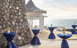 cocktail tables draped in navy tablecloths near a white gazebo overlooking the ocean